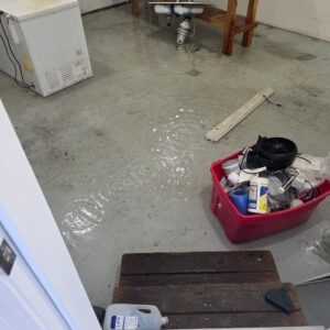 Water on the floor beneath an open kitchen sink cabinet after a line failure